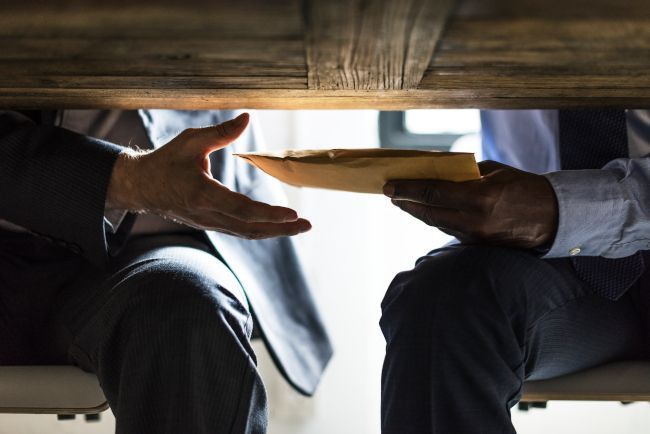 dos hombres pasándose un sobre bajo la mesa